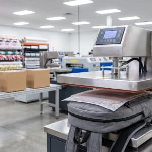 In Logo Lên Balo: Hướng Dẫn Chi Tiết Cho Chủ Shop & Doanh Nghiệp Máy in chuyển nhiệt đang in logo lên balo tại xưởng INTERPRINT